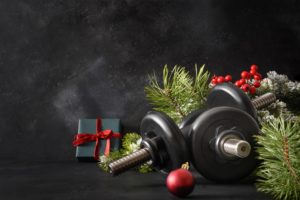 Christmas sport composition with blue sports dumbbells, gift, fir tree branches and Christmas gift